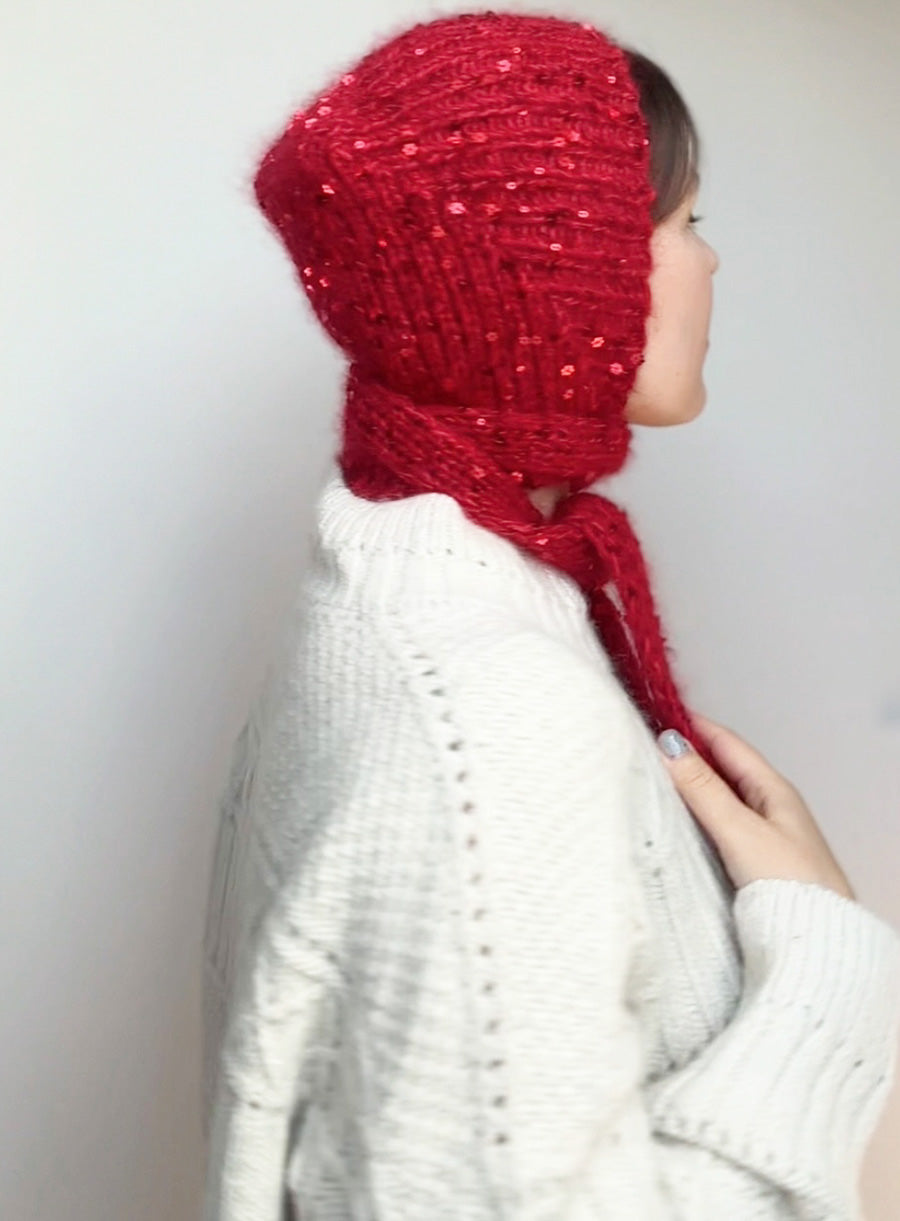 Chic and unique hand-knitted bonnet in red, embellished with tiny sequins. Modeled on a woman, styled for a fairy tale or rustic autumn wardrobe.
