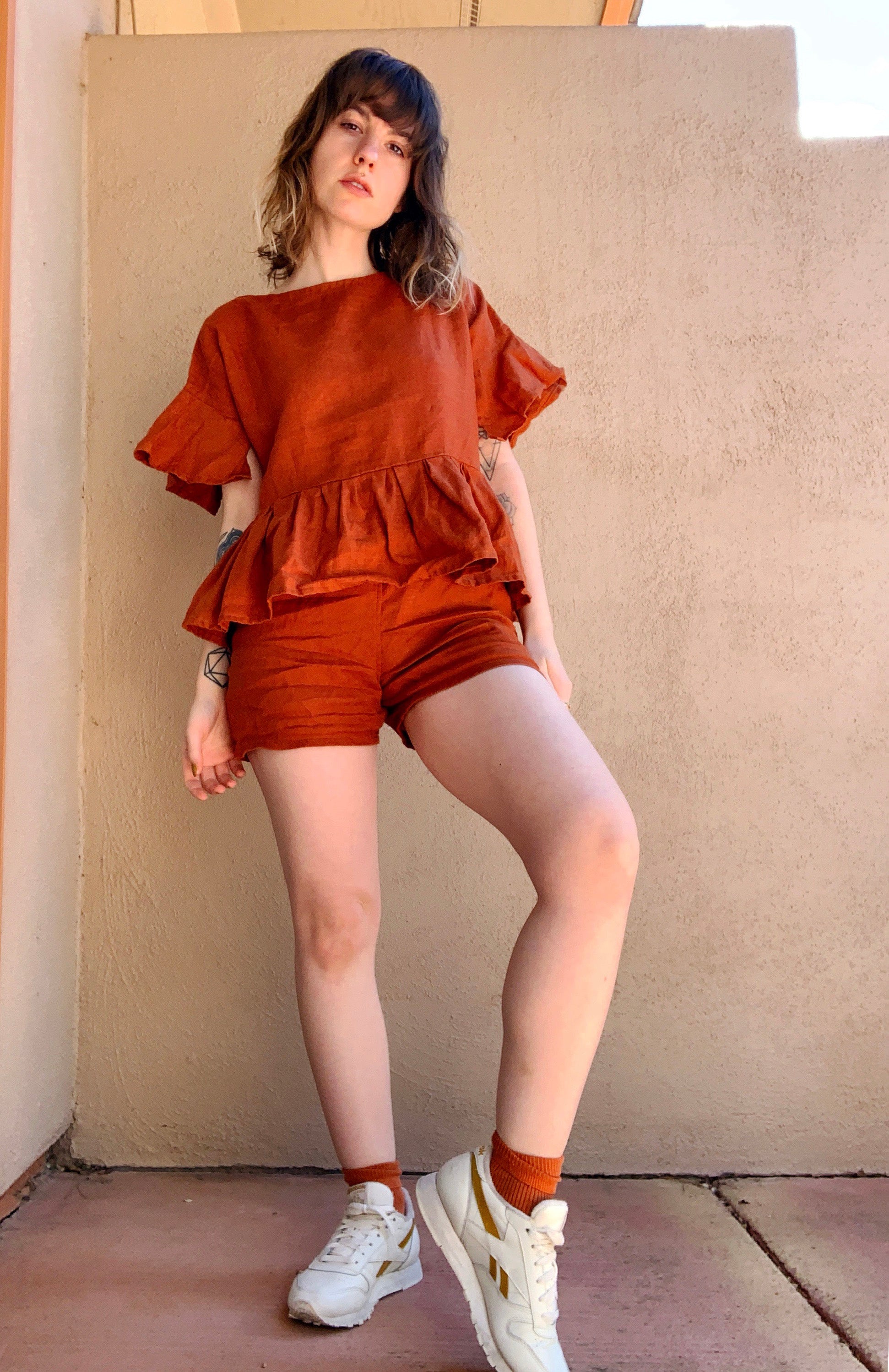 Fashionable rust-colored linen loungewear set with a ruffled peplum top and shorts, styled casually