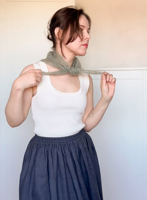 Woman wearing a white tank top and blue skirt holding a green knitted scarf.