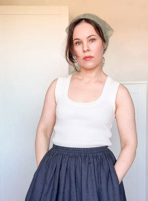 Woman wearing a white tank top and dark blue skirt with a light background