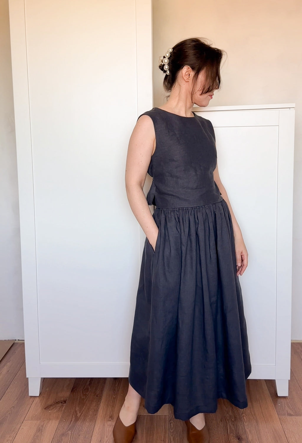 Woman wearing a sleeveless black top and a gathered midi-length black linen skirt, standing indoors on a wooden floor