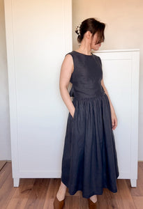 Woman wearing a sleeveless black top and a gathered midi-length black linen skirt, standing indoors on a wooden floor