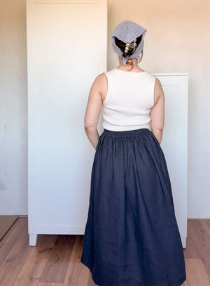 Person wearing a white sleeveless top and navy blue skirt with a patterned headscarf indoors.