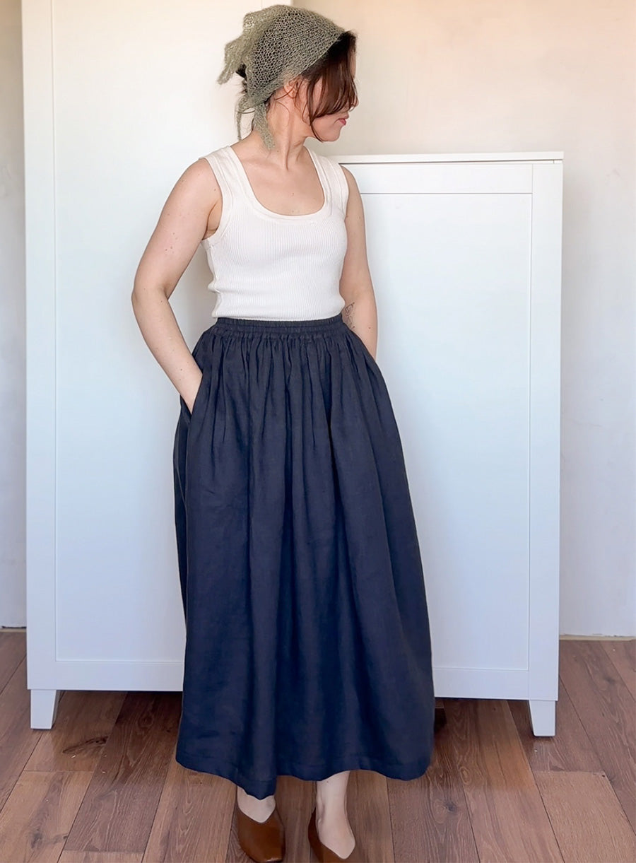 Woman wearing a white tank top and navy blue skirt with a patterned headscarf indoors.