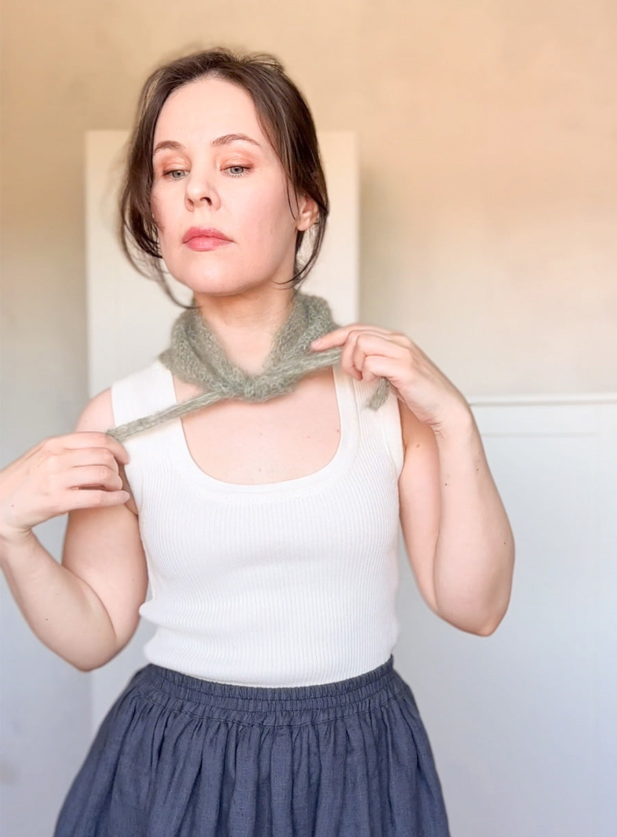 Woman wearing a white tank top and blue skirt, holding a green knitted scarf.